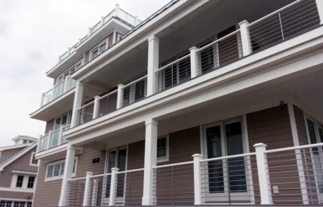 Side of a home with brown siding, VueTube on the first and second floor porch and glass railing on the bedroom balcony and other balconies. Cellular PVC posts on all railing. Closer camera shot of VueTube Railing.