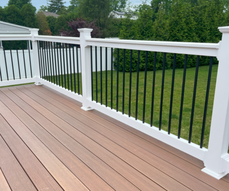 Black Round Balusters with PVC Railings on a brown deck in a backyard with green grass.